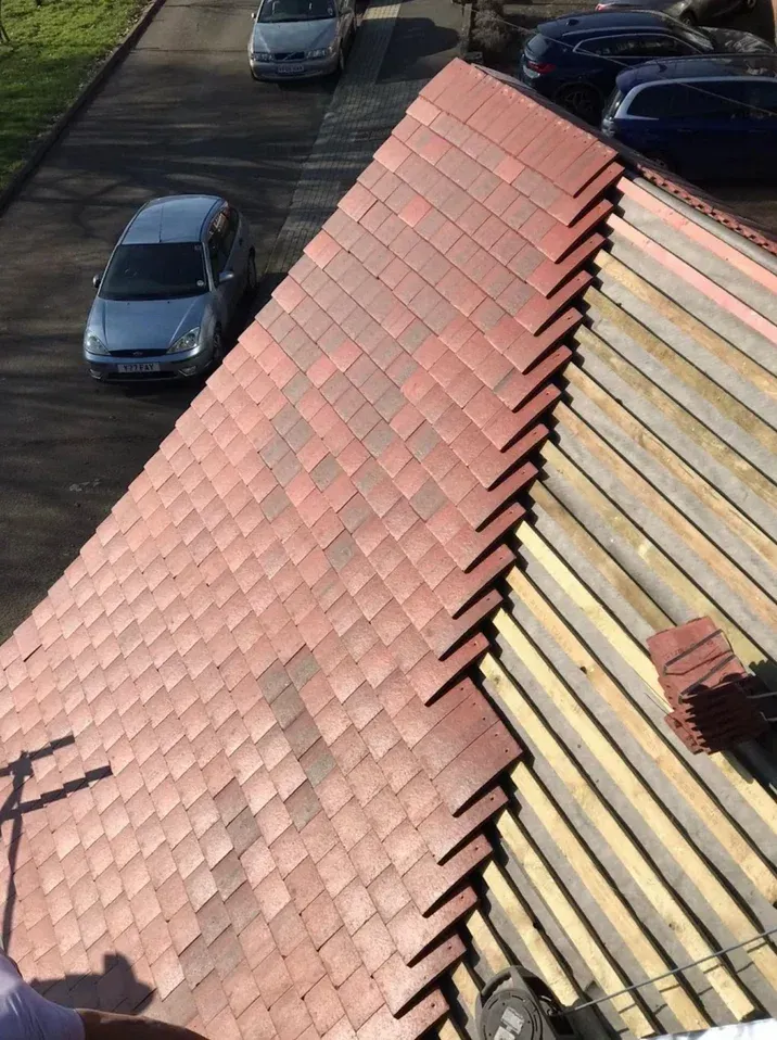 Damaged red-tiled roof with missing tiles exposing the underlayment beside parked cars