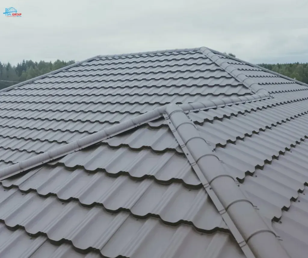 Gray tiled metal roof with ridge caps, viewed from above against a cloudy sky and trees