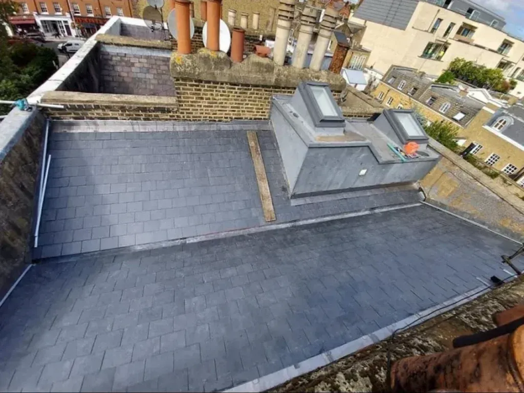Rooftop with dark gray slate tiles, chimneys, and a small rooftop structure in an urban neighborhood