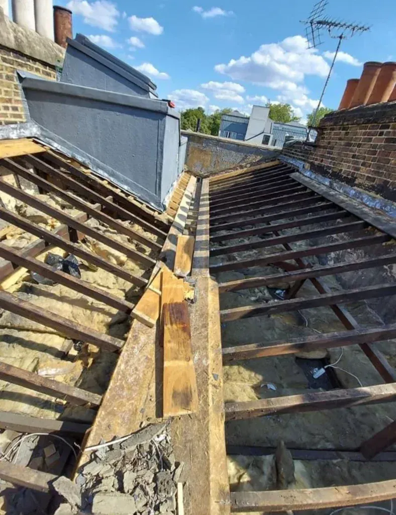 Partially stripped roof with exposed rafters and a narrow gap between two roof sections under a blue sky