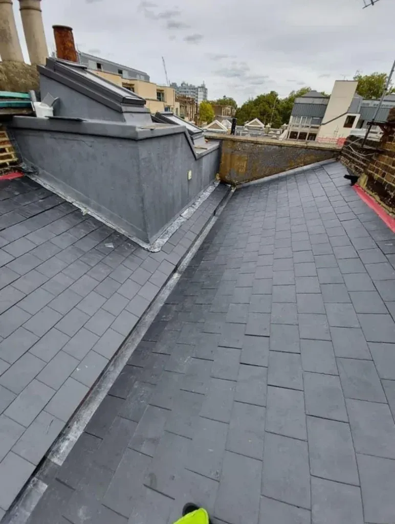 Rooftop with gray shingles, low walls, and surrounding buildings under an overcast sky