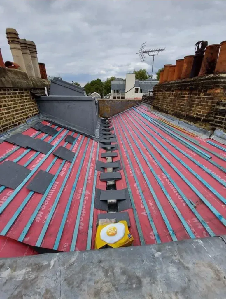 Rooftop with red-and-gray striped roofing felt and multiple brick chimneys under a cloudy sky