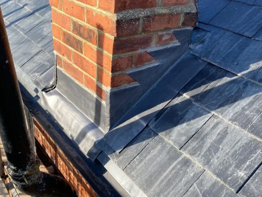 Close-up of a brick chimney with lead flashing on a dark shingled roof