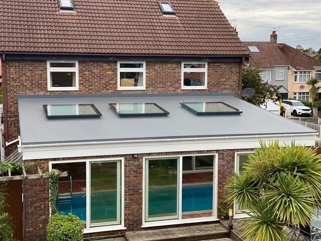House with a gray roof, three skylights, and a glass-enclosed rear extension with pool inside