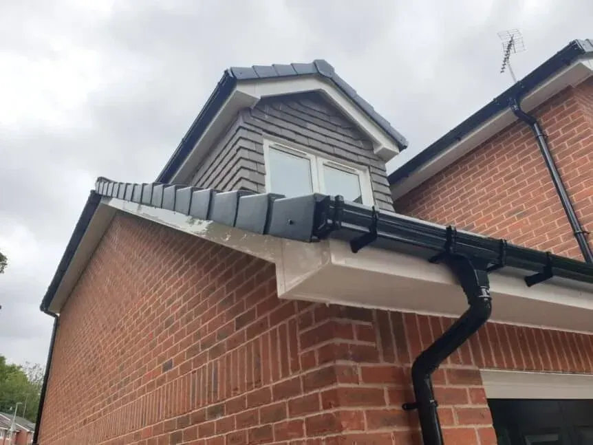 Brick house corner with dark gray gutter and downspout beneath a dormer window