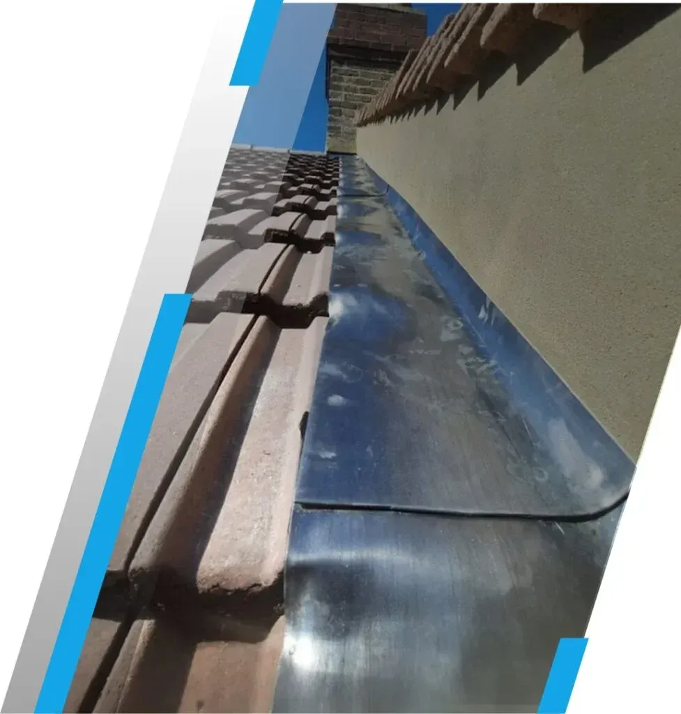 Tilted view of a roof gutter, blue sky reflection on metal flashing, and beige stucco wall with brown trim.