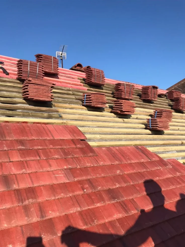Red roof under repair with stacked red tiles on a sloped roof against a clear blue sky