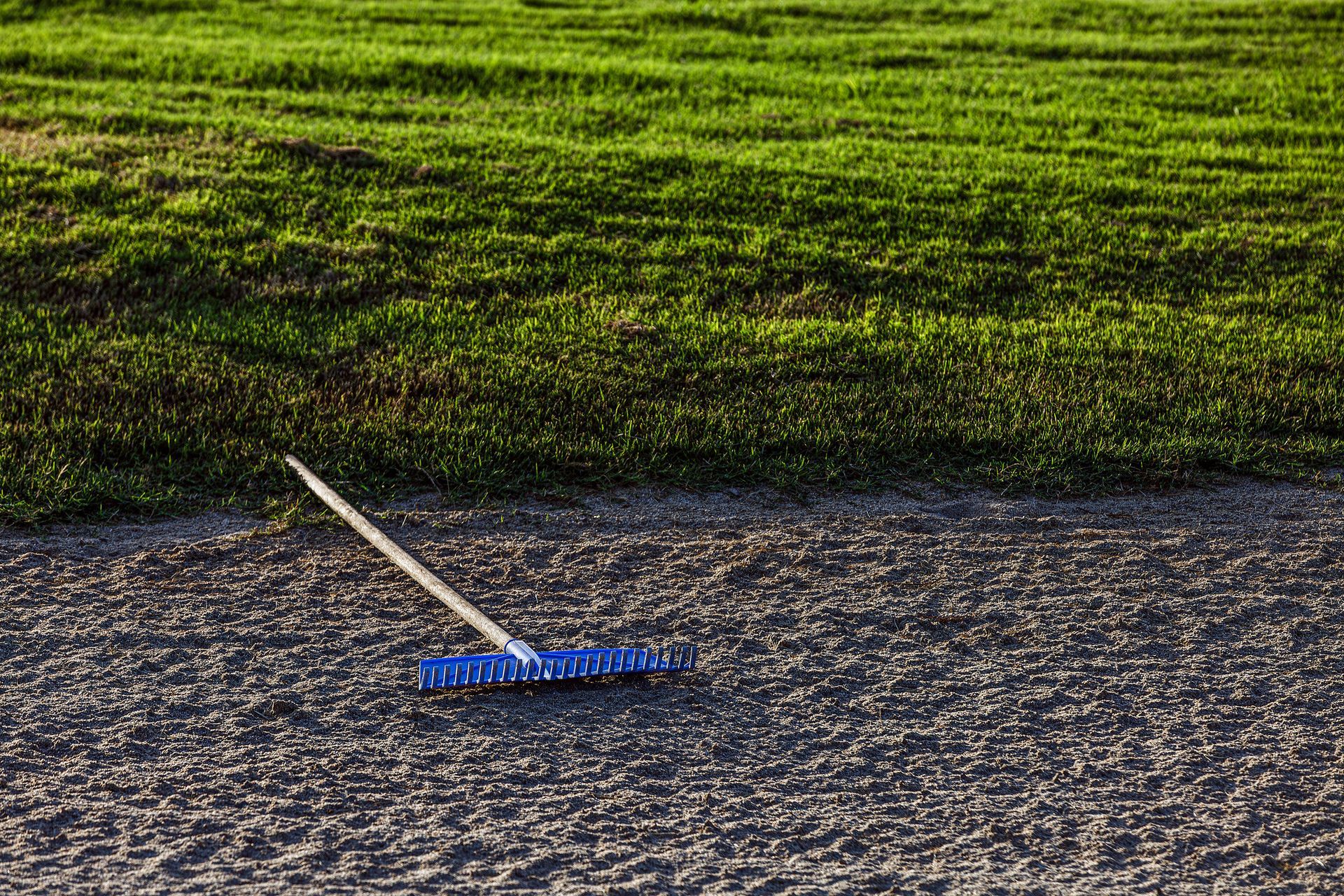 Blue rake on textured sand next to a grassy hill.