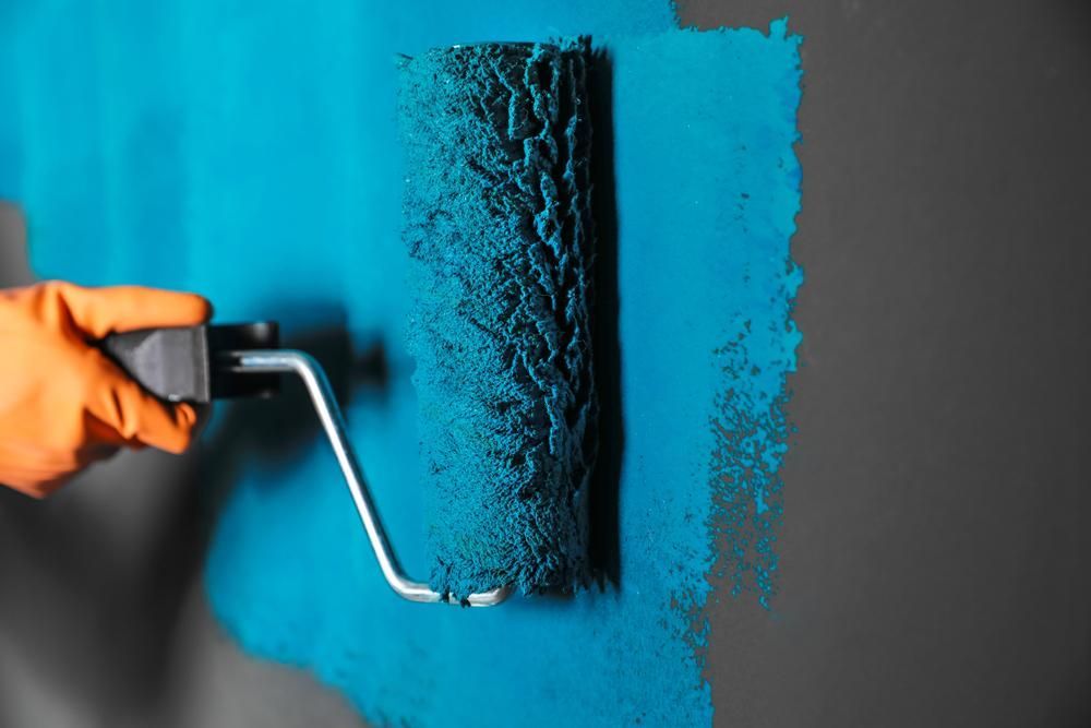 A Person Is Painting A Wall With A Blue Paint Roller — Donnelly Painting In Yamba, NSW
