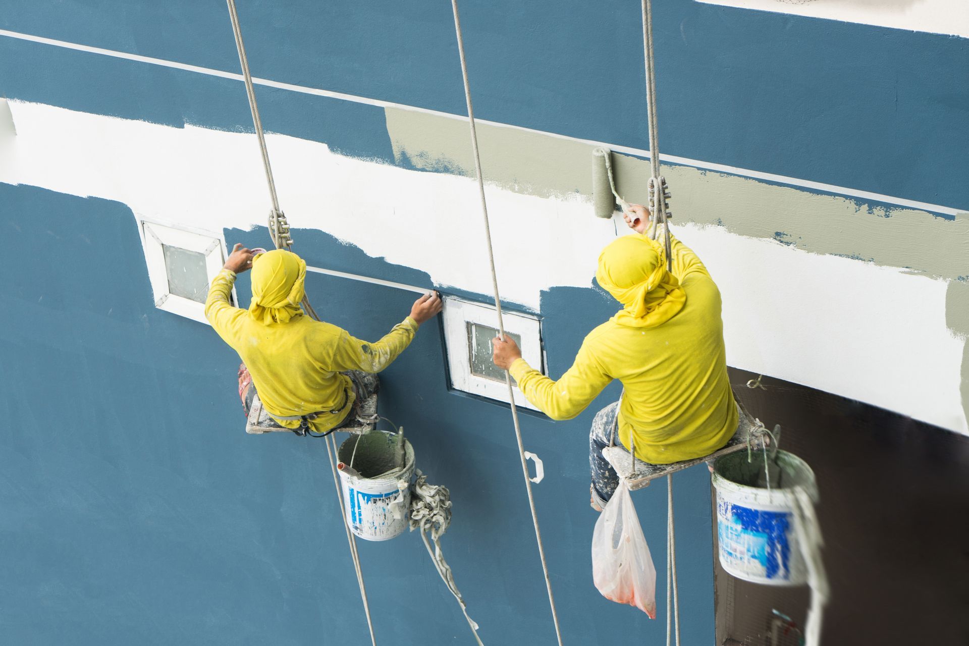 Two men are painting a wall with buckets attached to ropes.