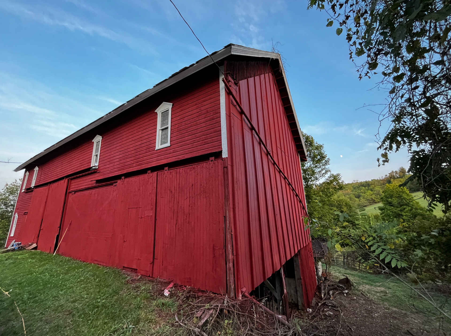 A large red barn is sitting in the middle of a grassy field.