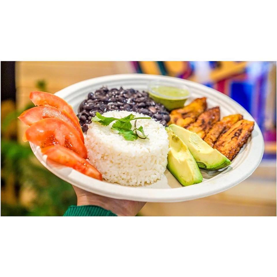 A person is holding a plate of food with rice , beans , tomatoes and avocado.