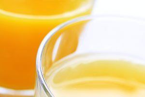 A close up of two glasses of orange juice on a table.