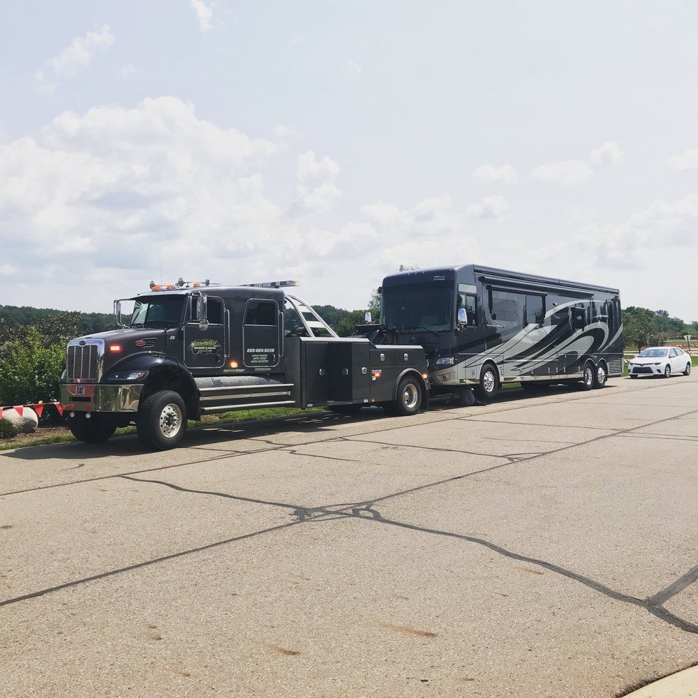 Tow truck towing a large RV on asphalt under a cloudy sky.