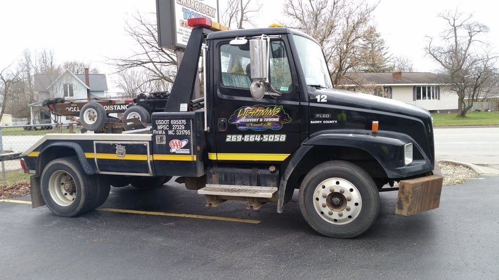 Black tow truck parked on asphalt; business name on the door.