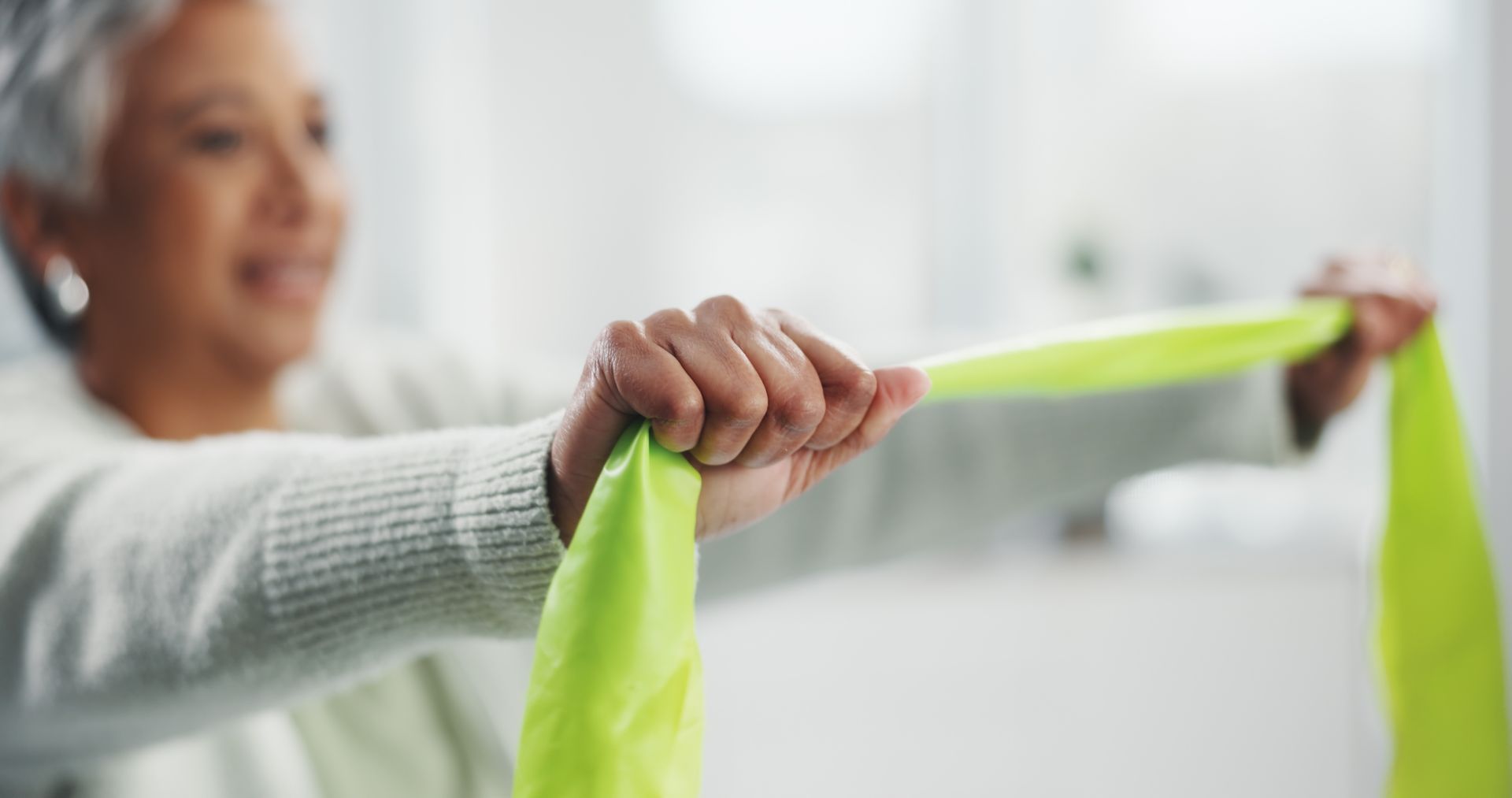 Woman stretching a bright green resistance band in a bright indoor room