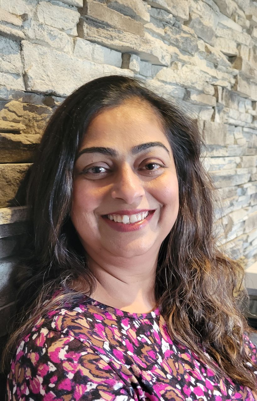 A woman in a purple shirt is smiling in front of a brick wall.