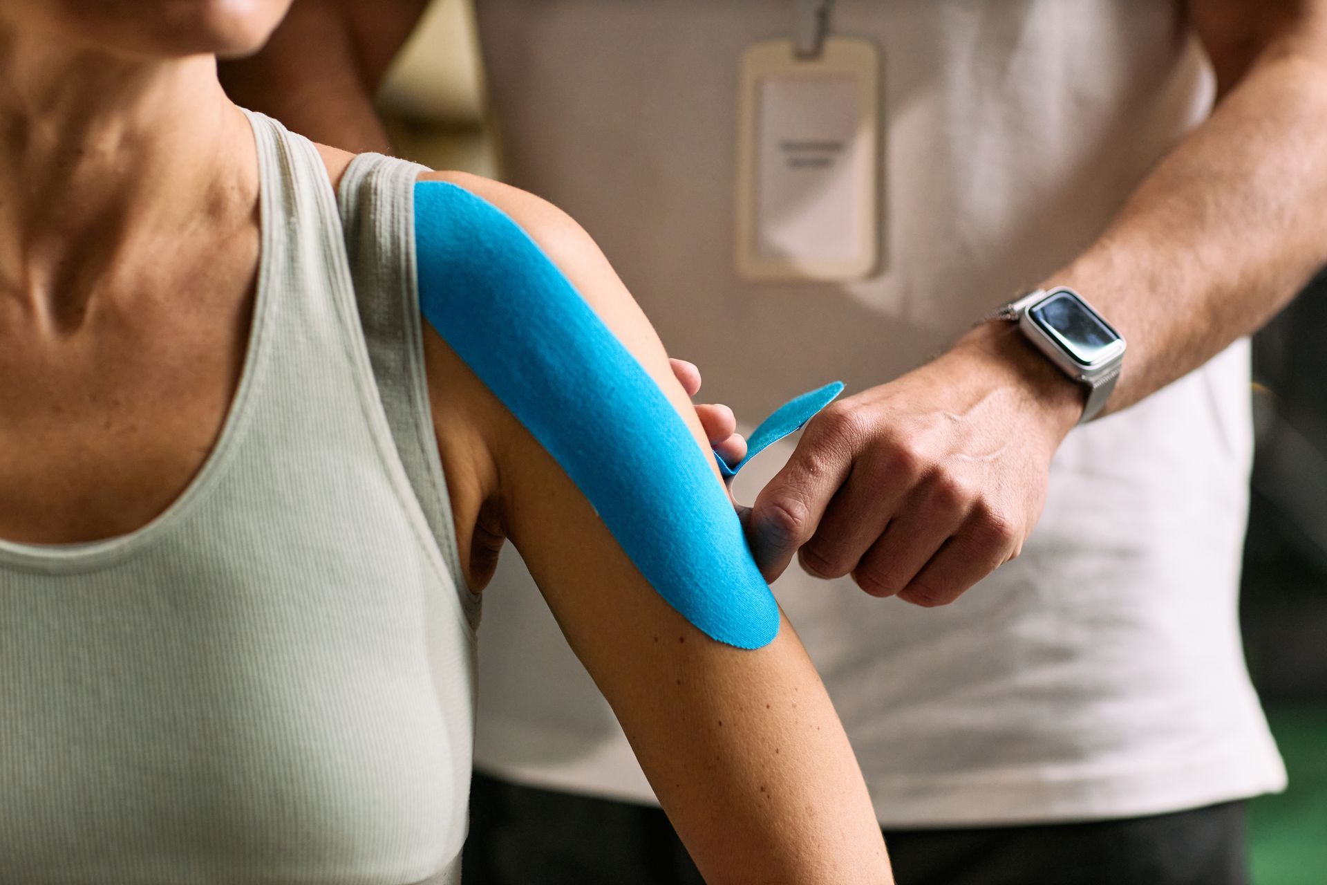Blue kinesiology tape being applied to a person’s upper arm by a clinician in a medical setting