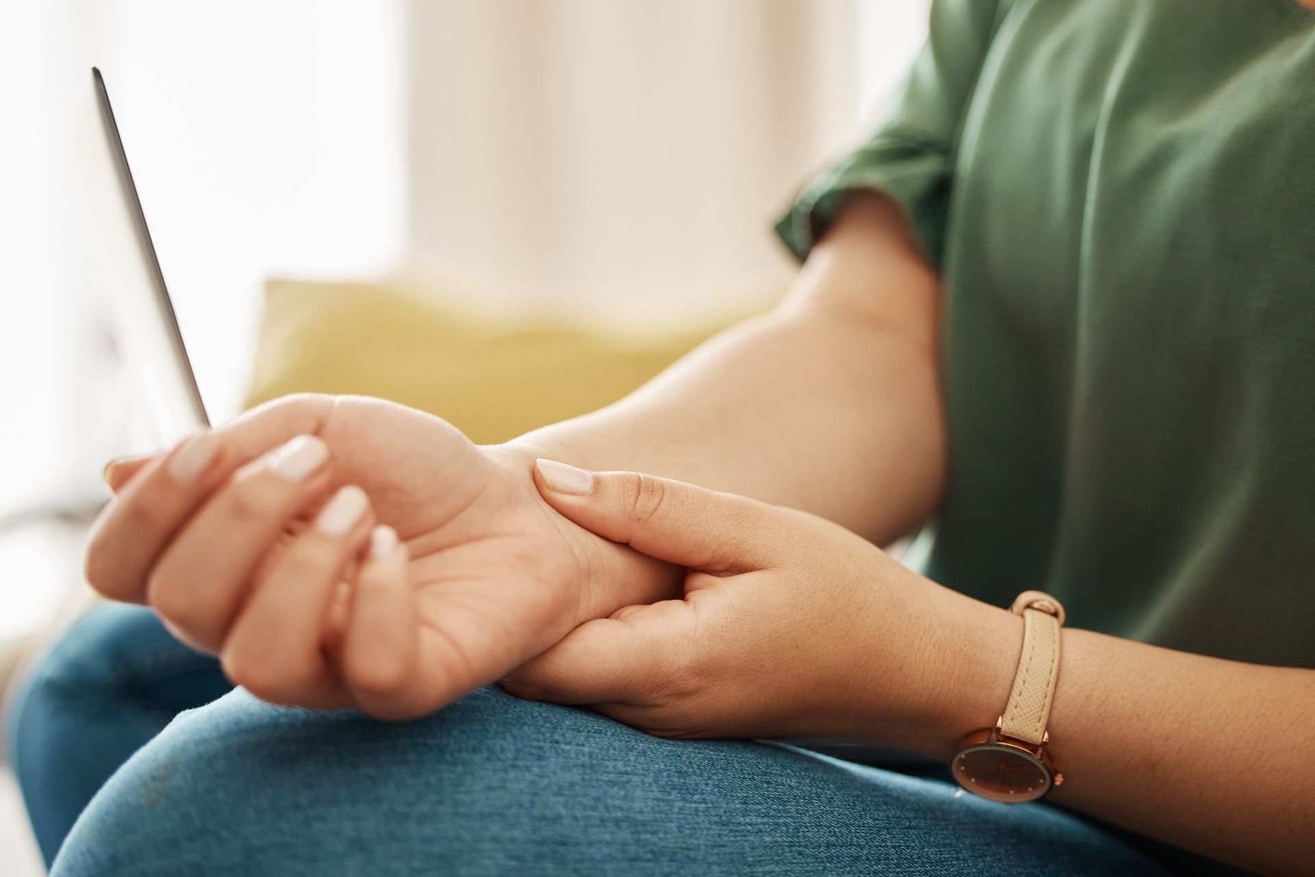 Person holding their wrist with a brown watch, seated in a green shirt and jeans.