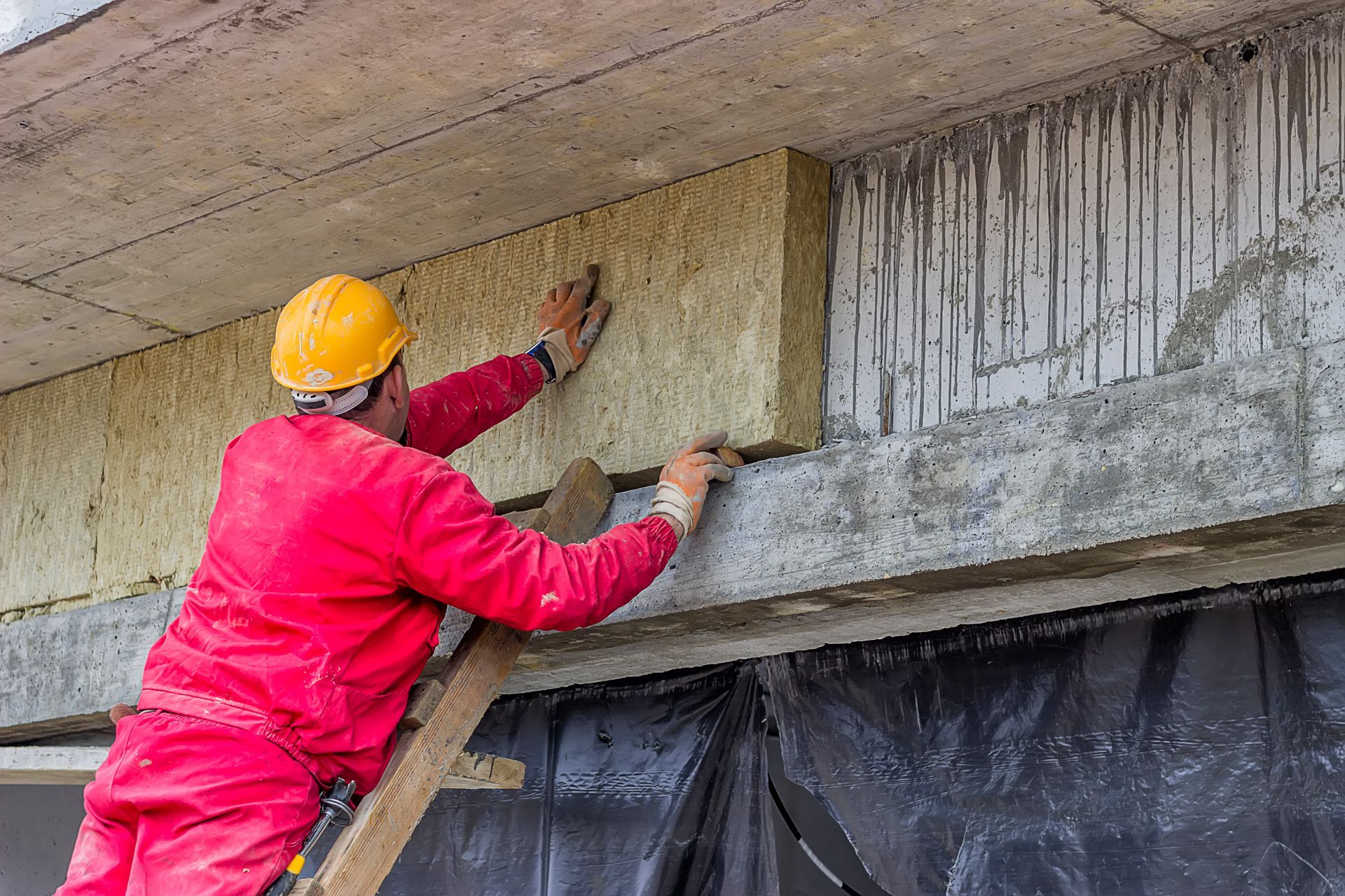 Un uomo è in piedi su una scala e sta installando l'isolamento su un edificio.