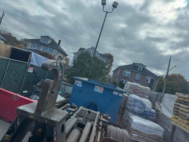 Heavy machinery in a construction area in stamford, with a blue dumpster under a cloudy sky.