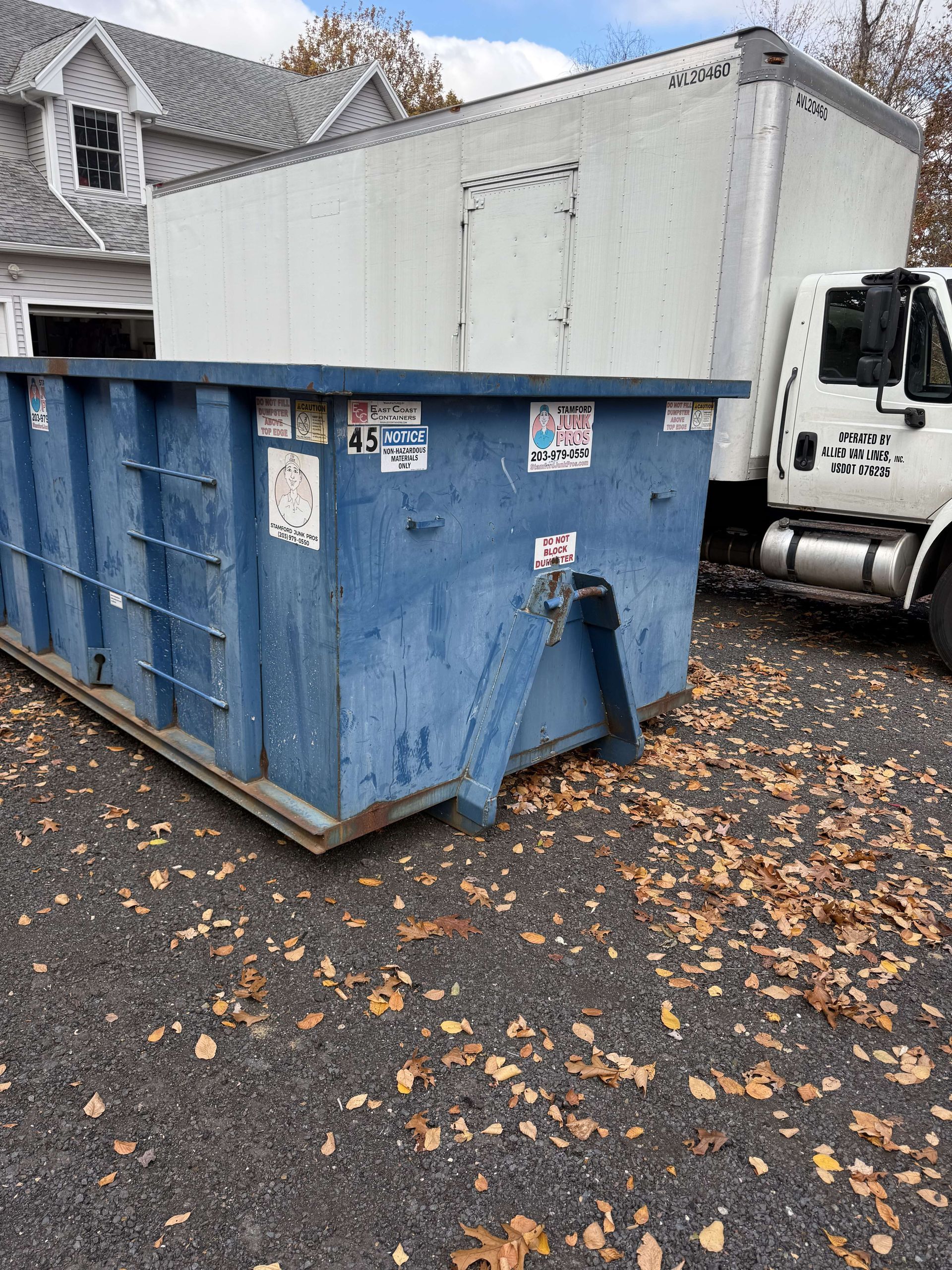 Blue dumpster and white truck parked on asphalt driveway, in front of a house in beacon falls