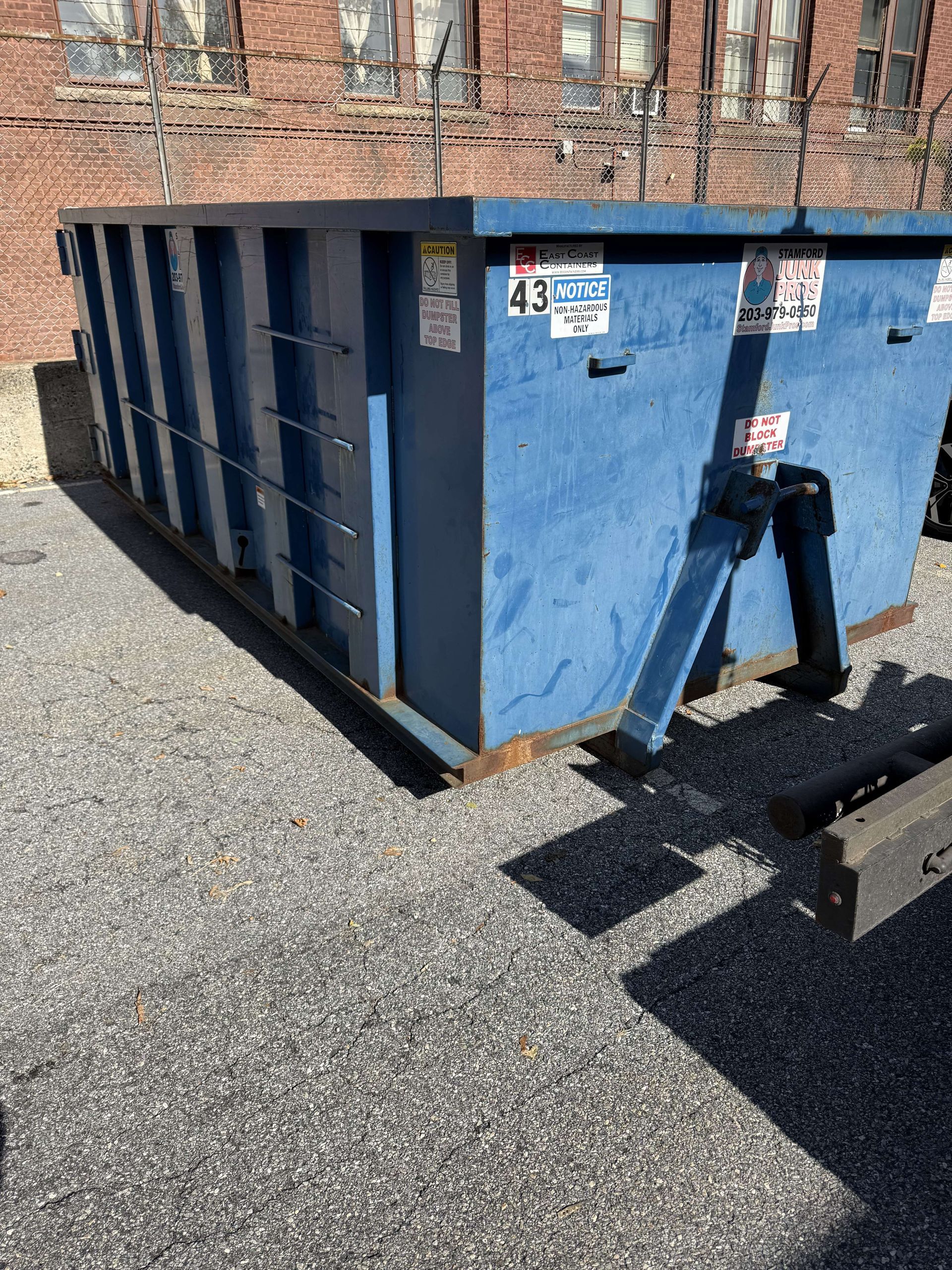 Blue dumpster in an outdoor lot, next to a building.