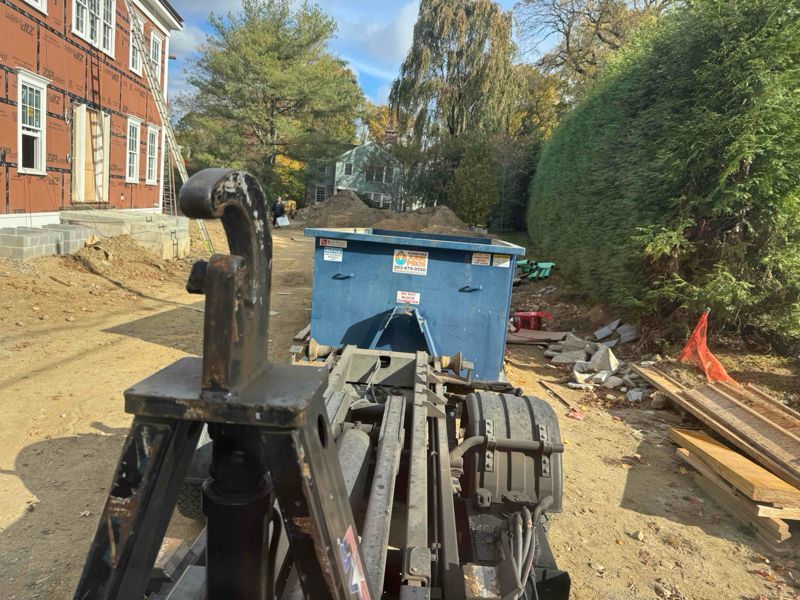 Forklift next to a blue dumpster filled with dirt, construction site, daytime.