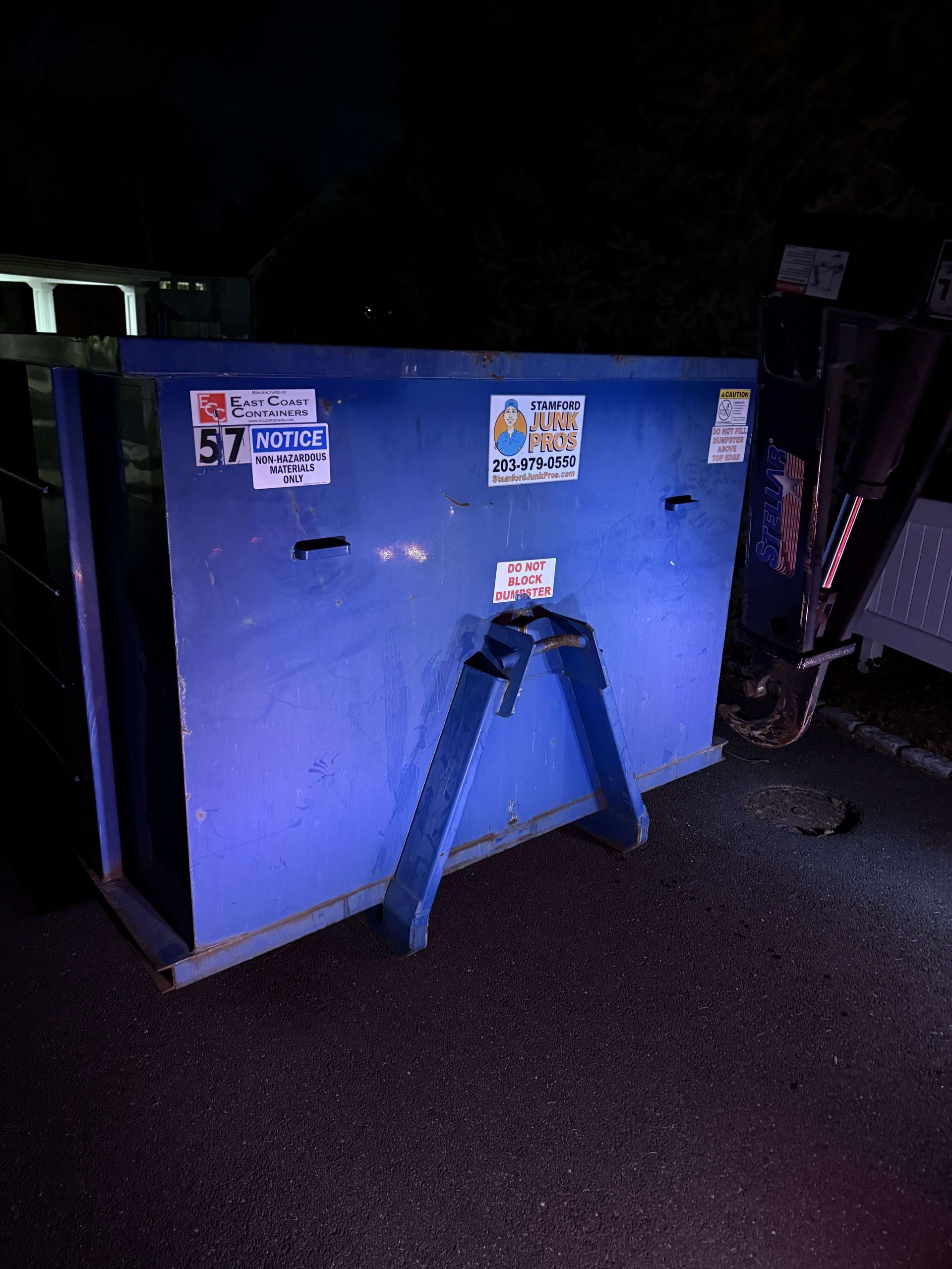 Blue dumpster with support frame, against a dark background.