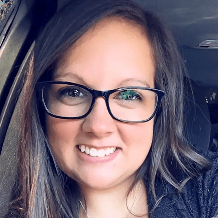 A woman wearing glasses is smiling while sitting in a car.