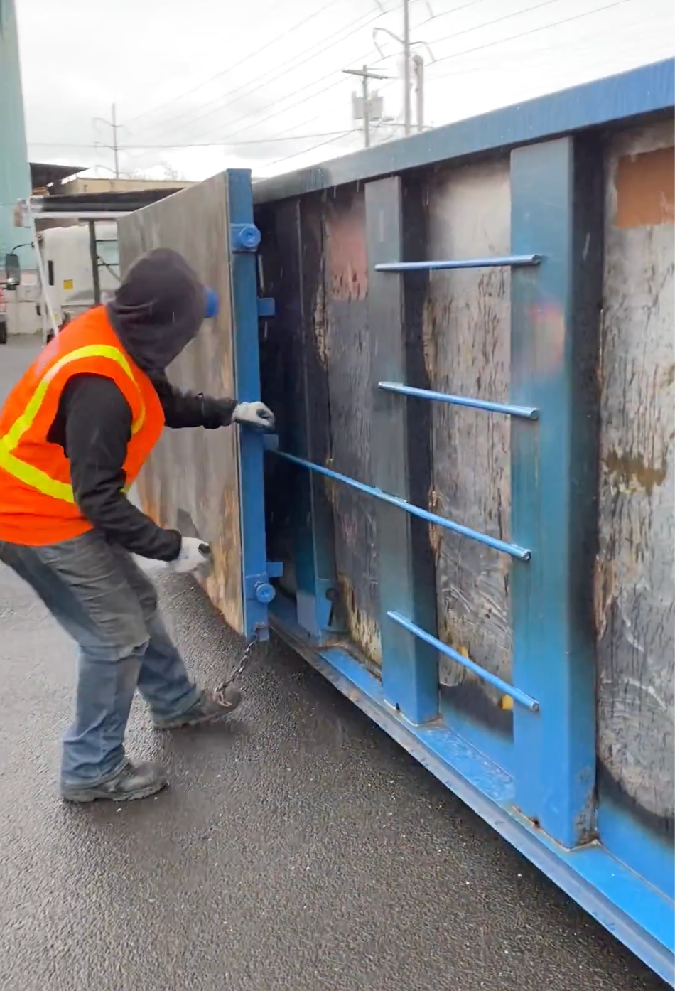 Person in orange vest opening a blue dumpster. Outdoors, overcast. fire damage dumpster in stamford