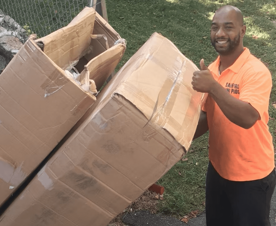 A man in an orange shirt is holding two cardboard boxes and giving a thumbs up.