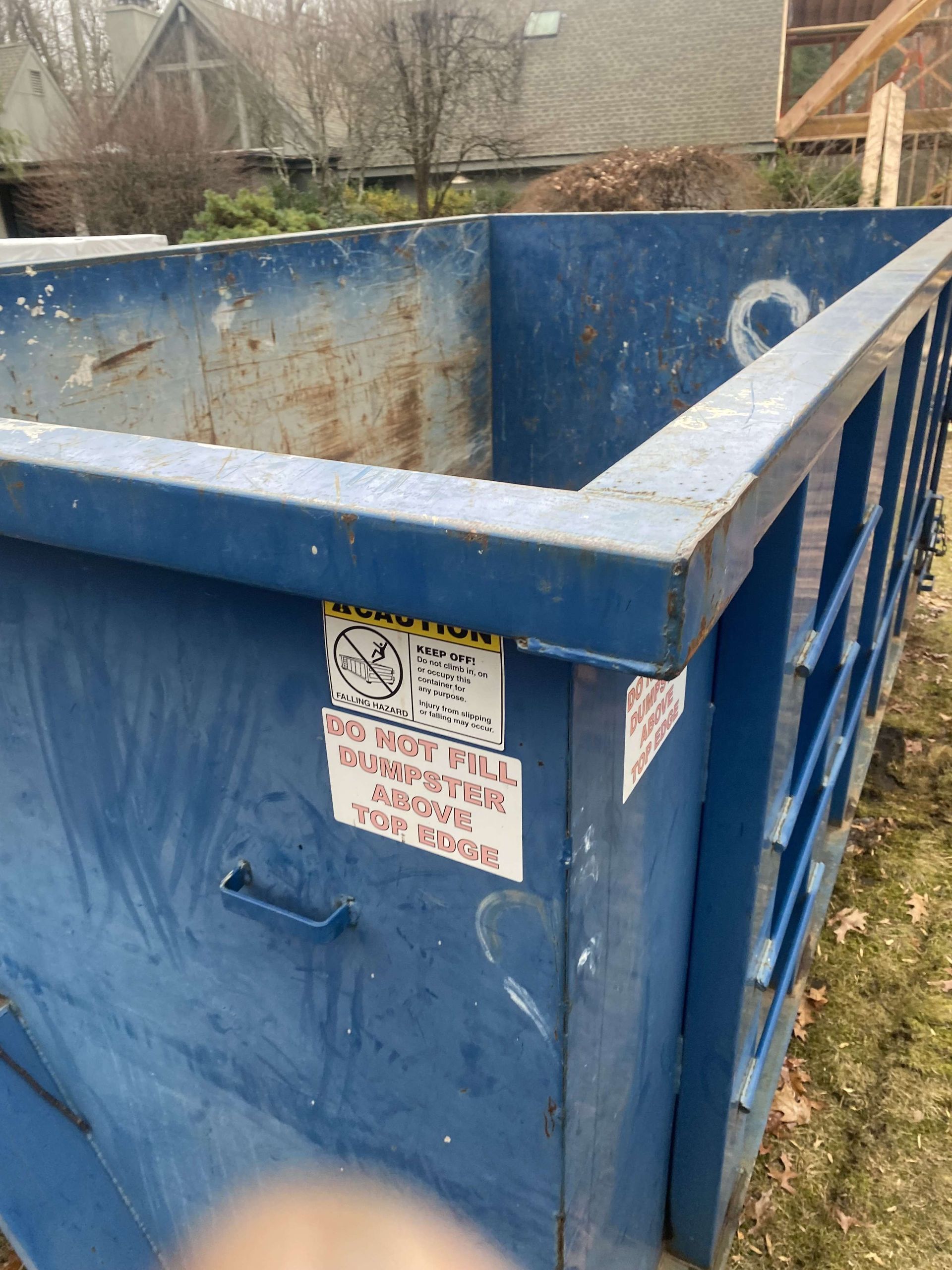 Blue metal dumpster outdoors with warning labels in white plains.