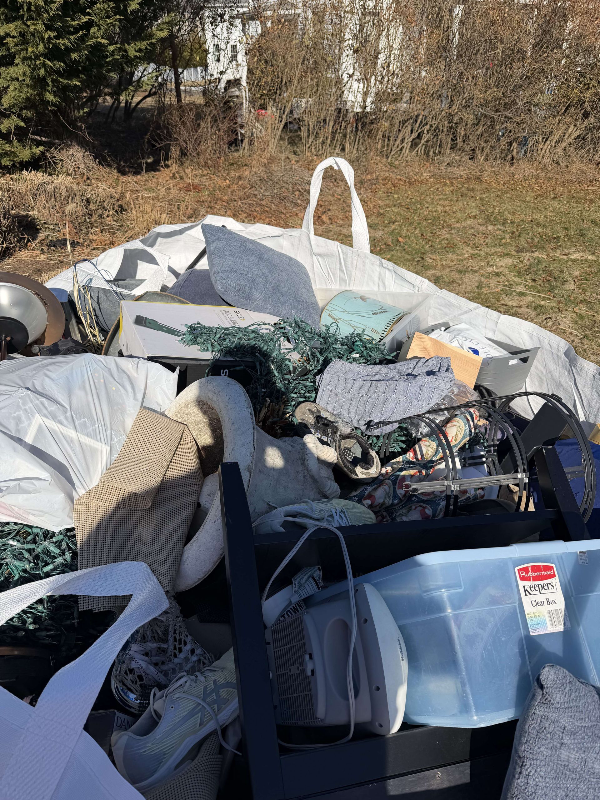 Pile of household items in grizzly bag covered by a white tarp, outdoors in a yard.