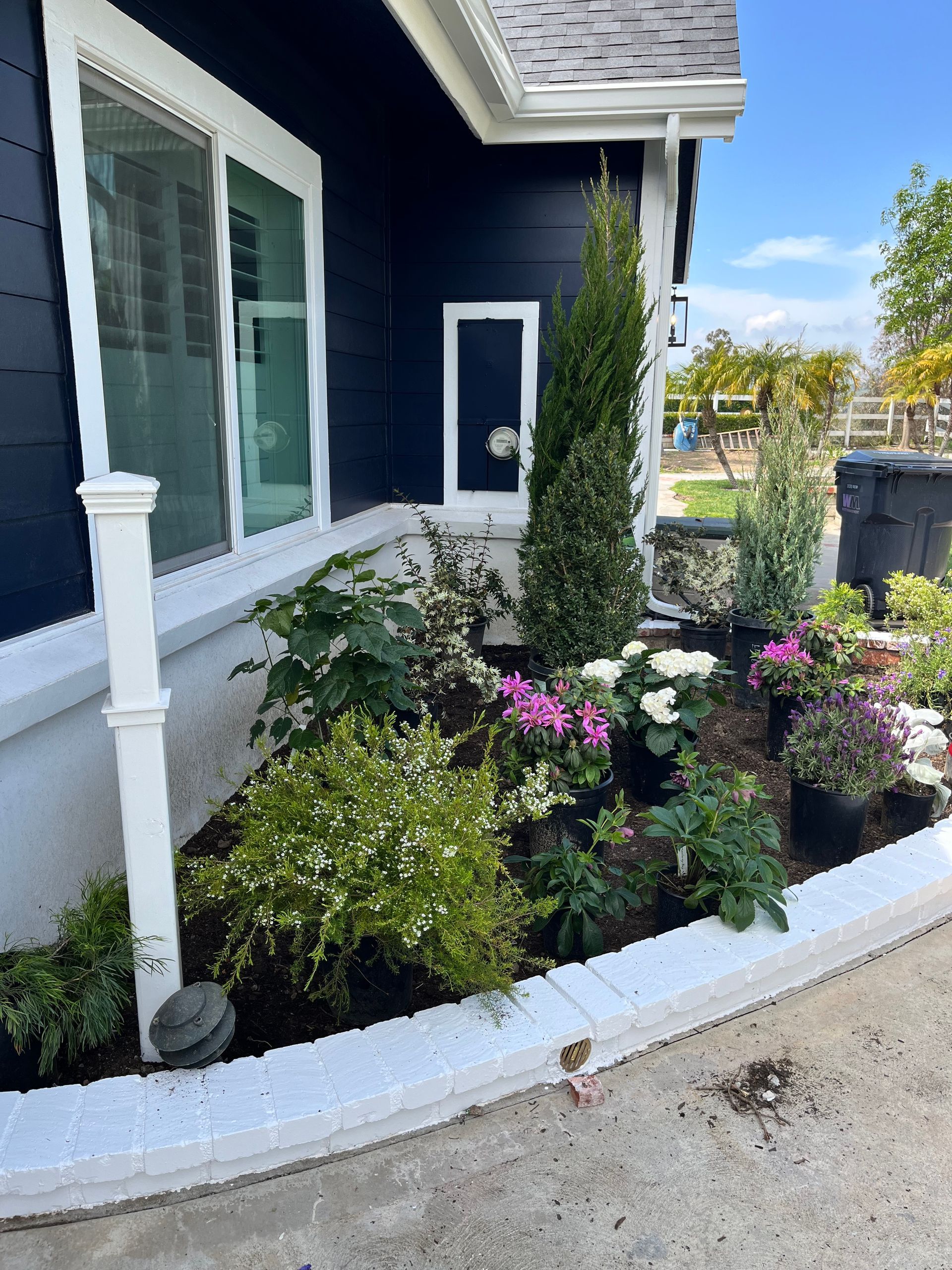 A black house with a white trim and a garden in front of it.