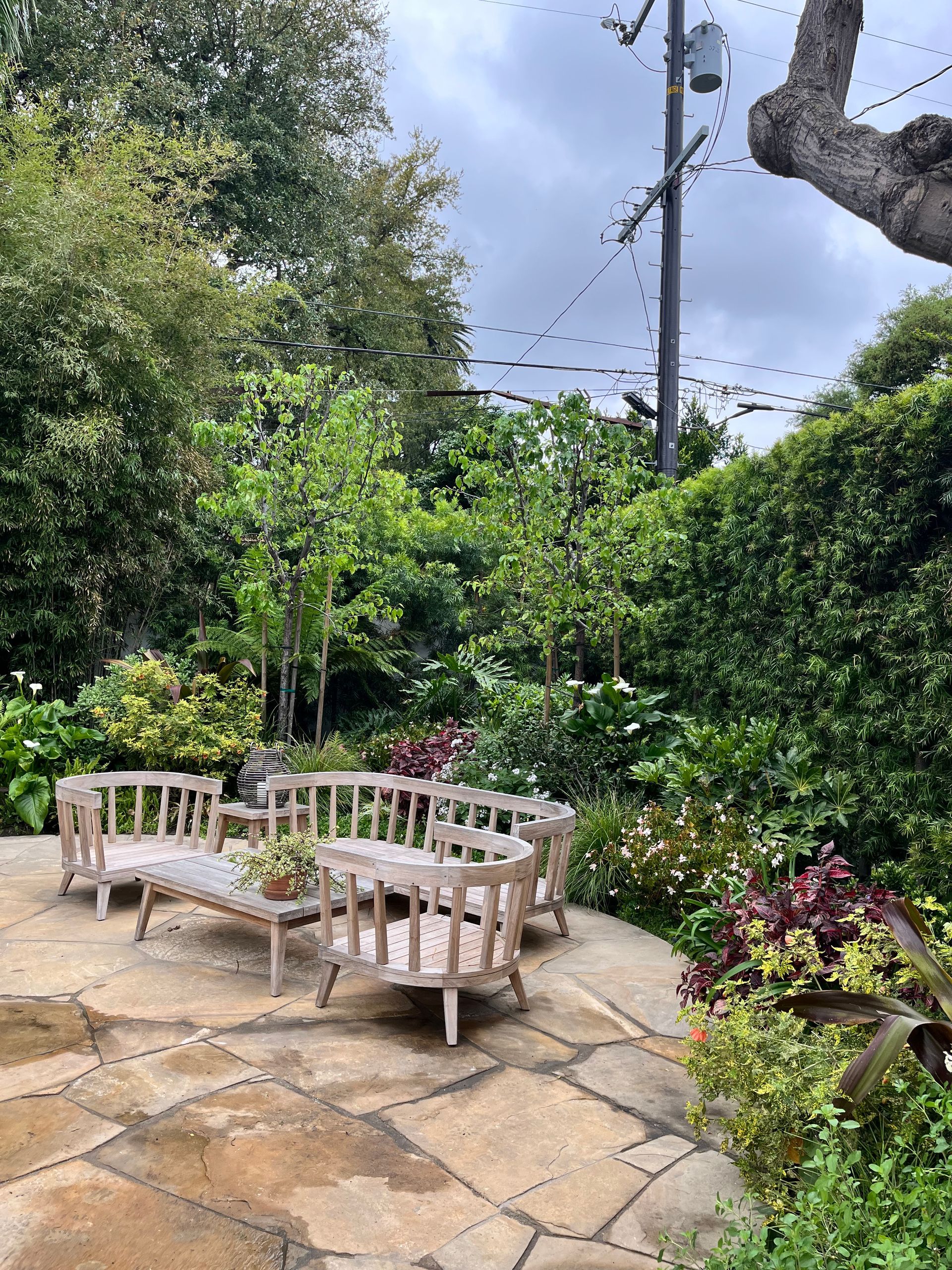 A patio with chairs and a table in a garden surrounded by trees.