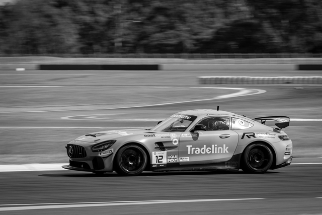 Black-and-white race car speeding on a track, with “TradeLink” branding visible on the side.