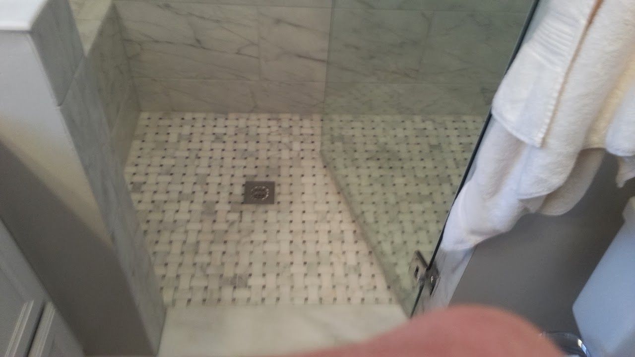 Shower with marble walls and mosaic tile floor, glass door, and towel hanging outside.