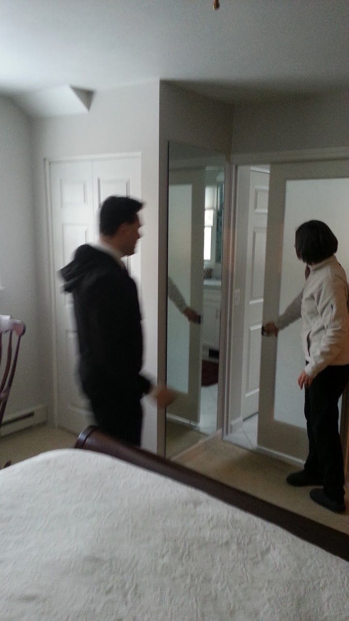 Person looking at a closet with frosted glass doors, another person opening the doors in a bedroom.