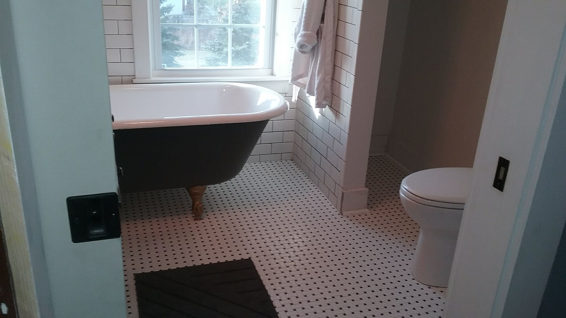Bathroom with clawfoot tub, toilet, and white tile floor. Sunlight streams through a window.