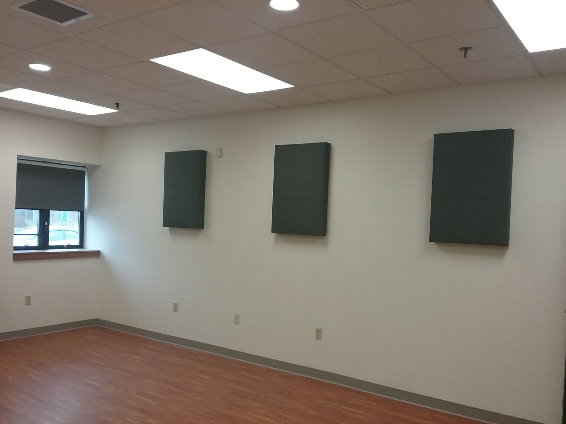Empty room with three sound-dampening panels on a white wall. Window on the left, wood-look floor.