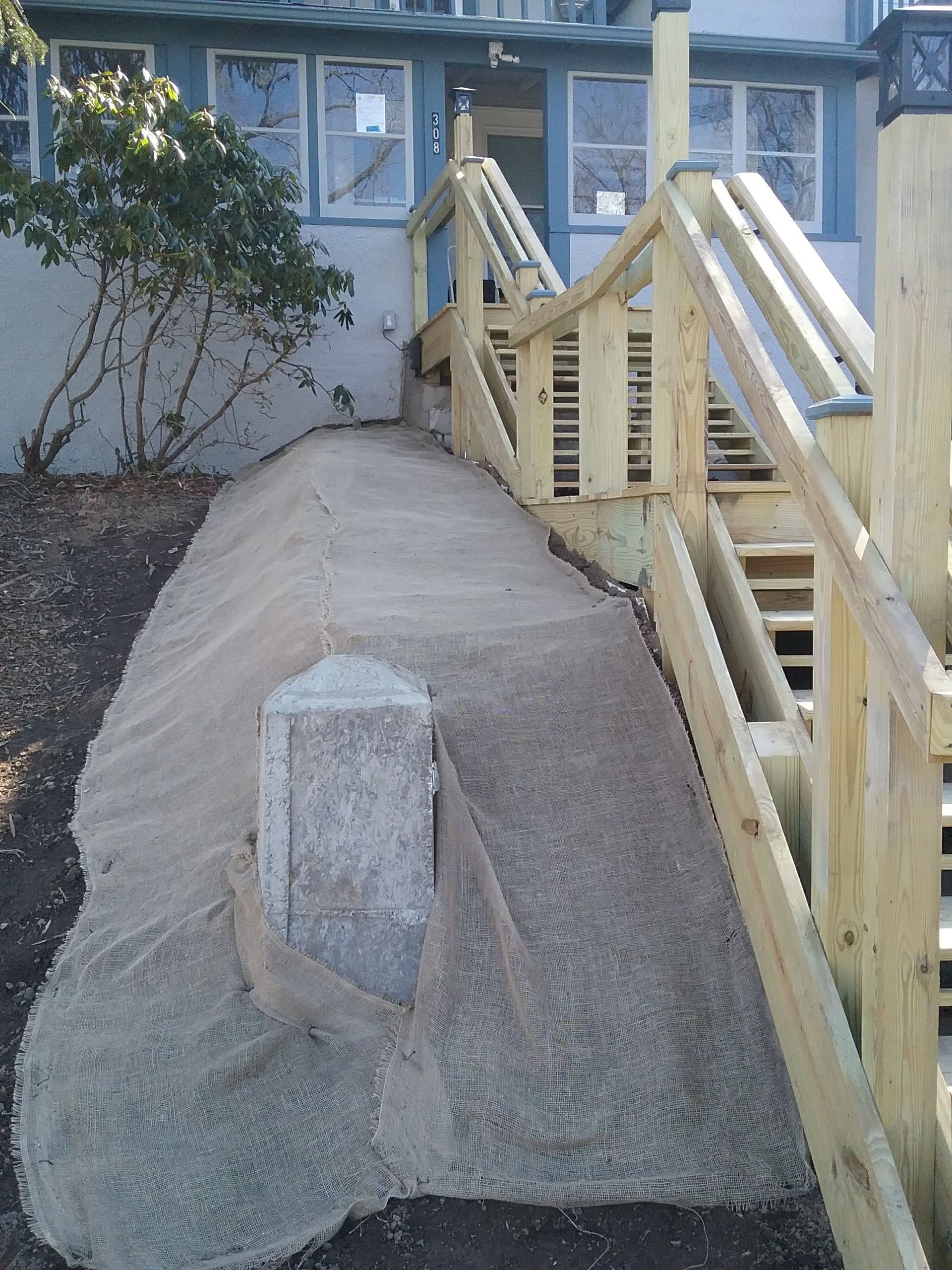 Concrete ramp leading to a house entrance with wooden stairs on the right. A mailbox sits in the ramp.
