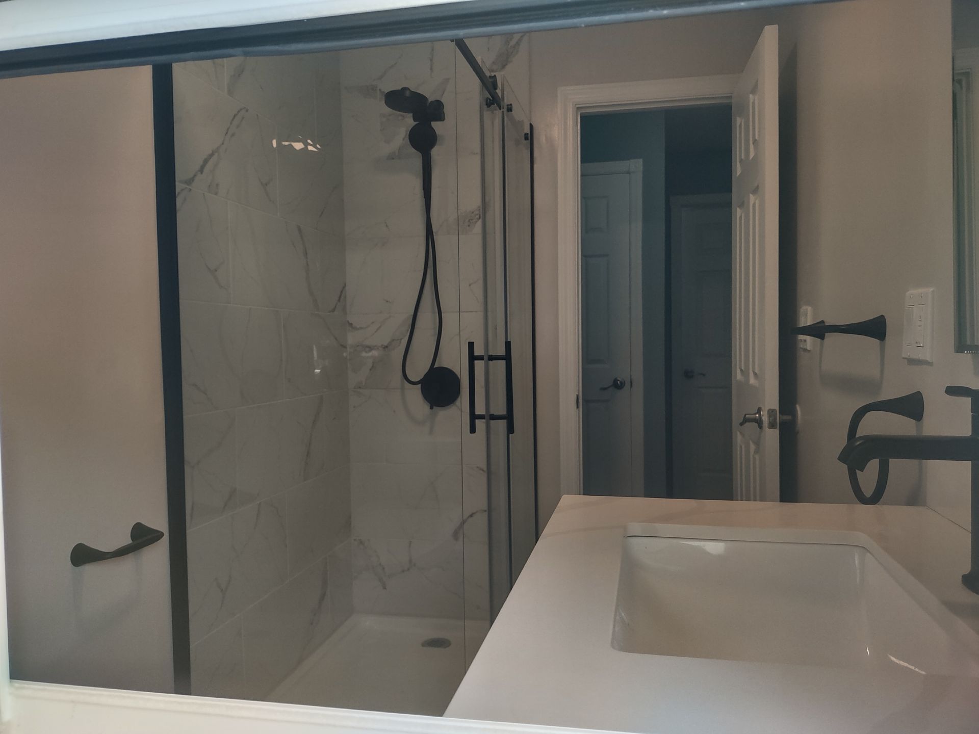 Bathroom with a white countertop, sink, and a glass shower with black fixtures.