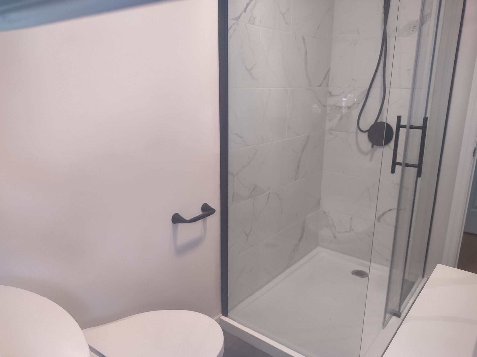 Bathroom with white walls, toilet, and a glass-enclosed shower with black fixtures.