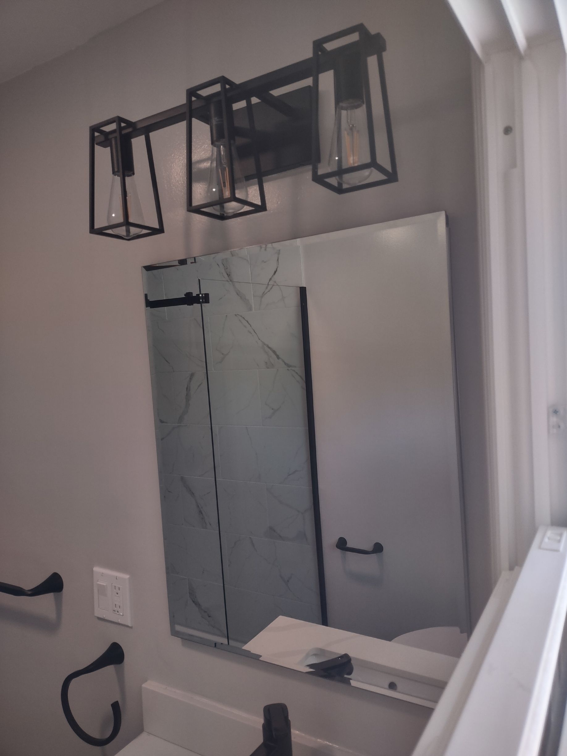 Bathroom with a mirror, black light fixture, and towel rack on a gray wall.