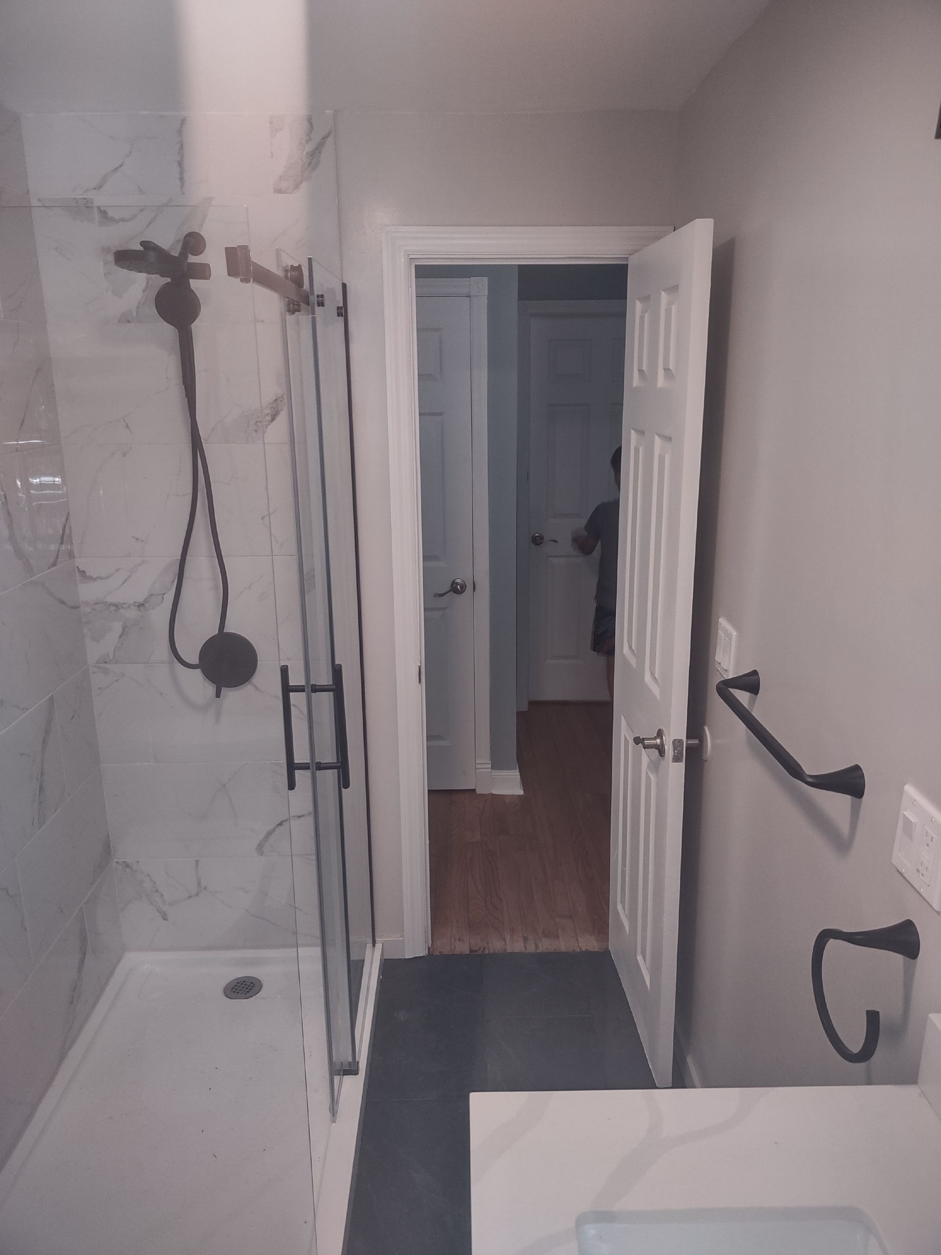 Bathroom with shower, open doorway, gray walls, and black fixtures.