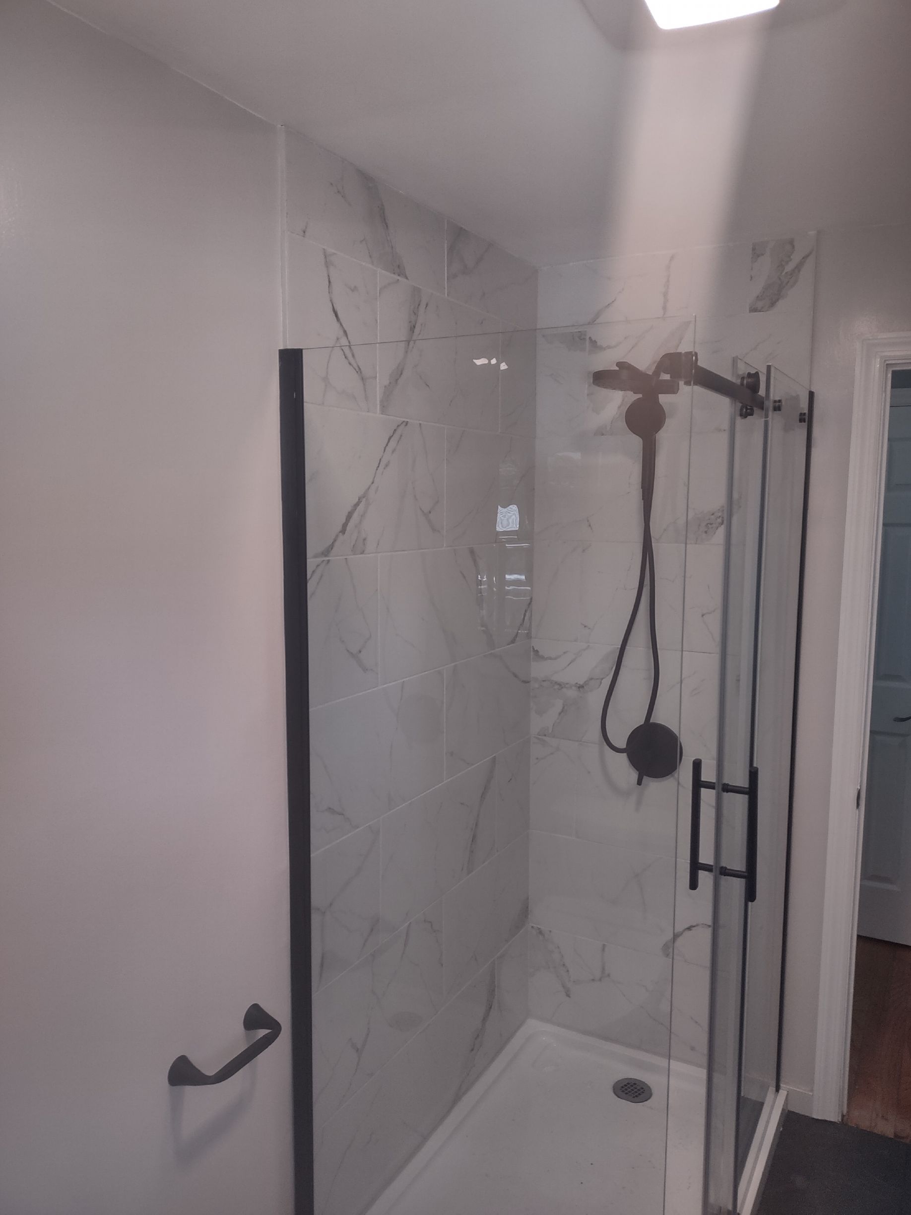 Modern shower with marble-look tiles, black fixtures, and glass door.