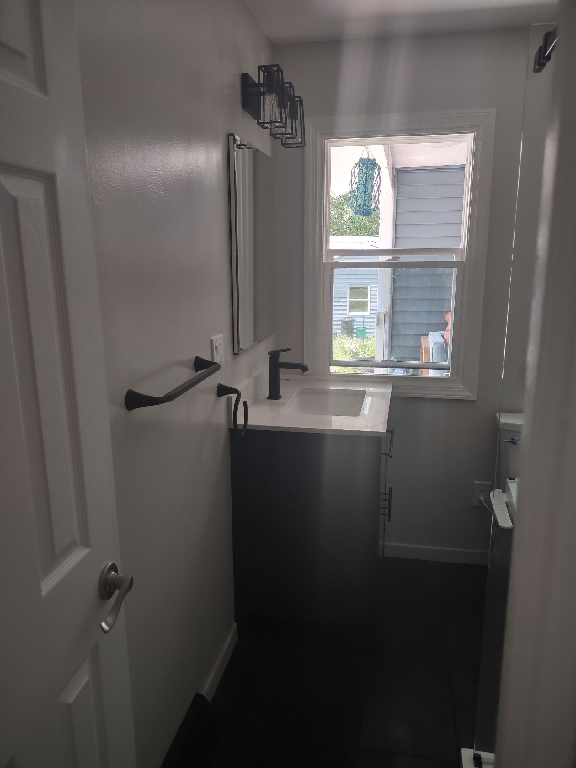 Small bathroom with vanity, sink, mirror, and window; dark floor and light gray walls.