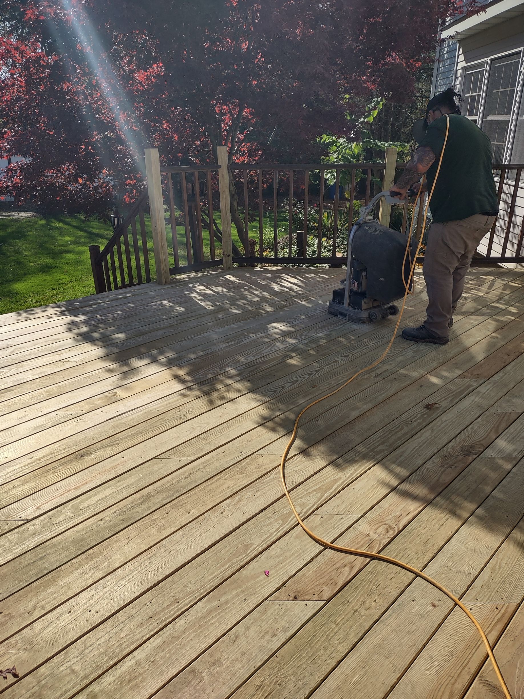 A man is sanding a wooden deck with a machine.