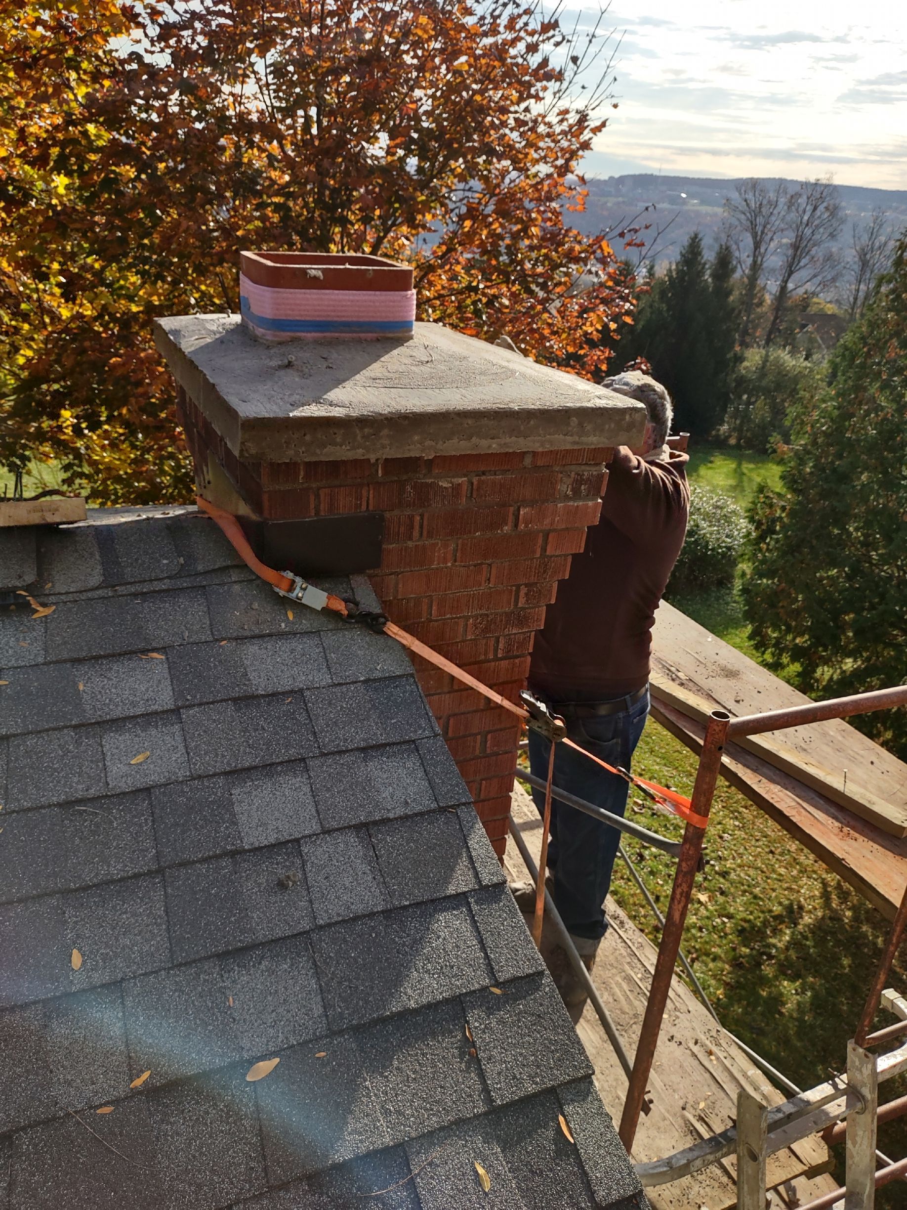 A man is standing on top of a roof next to a chimney.